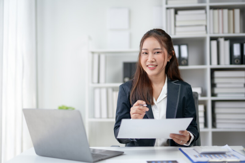 Confident businesswoman in a modern office setting, holding a document and smiling, showcasing professional work environment.