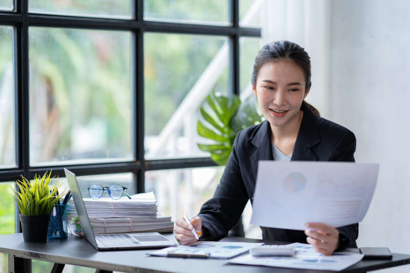 Asian businesswoman using a smartphone and planning, calculating Asian businesswoman using a smartphone and planning, calculating the budget Company expenses and income from charts, reports, finance, accounting, and laptop analysis.