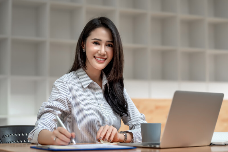 Charming young Asian businesswoman sitting at the office. Lookin Charming young Asian businesswoman sitting at the office. Looking at the camera.